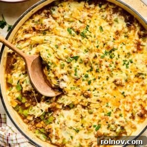 Cheese topped Philly cheesesteak skillet mixture in pan with wood spoon.