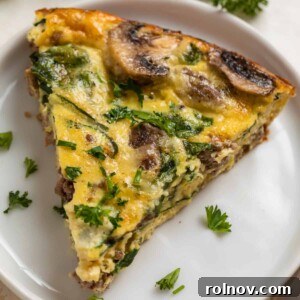 A generous slice of crustless mushroom quiche, showcasing savory beef, creamy Swiss cheese, and fresh spinach, garnished with chopped parsley and chives on a white plate.