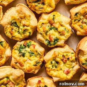 A selection of perfectly baked mini quiches made with flaky puff pastry, beautifully arranged on a plate and garnished with fresh onion and chopped parsley.