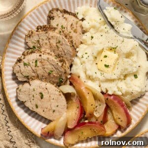 Sliced pork tenderloin served on a plate with tender roasted apples and creamy mashed potatoes, creating a complete and comforting meal.