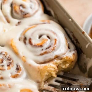 Golden brown iced buttermilk cinnamon rolls in a baking pan, ready to be served with a spatula.