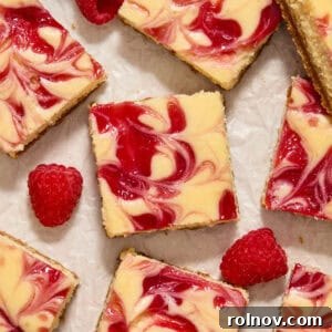 Beautifully arranged raspberry swirl white chocolate cheesecake bars on a surface, adorned with fresh, ripe raspberries.