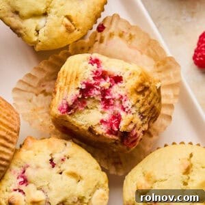 Beautifully baked white chocolate raspberry muffins, golden brown and speckled with fruit and chocolate chunks.