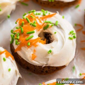A baked carrot cake donut with a swirl of cream cheese icing, adorned with festive sprinkles and delicate shredded carrots.