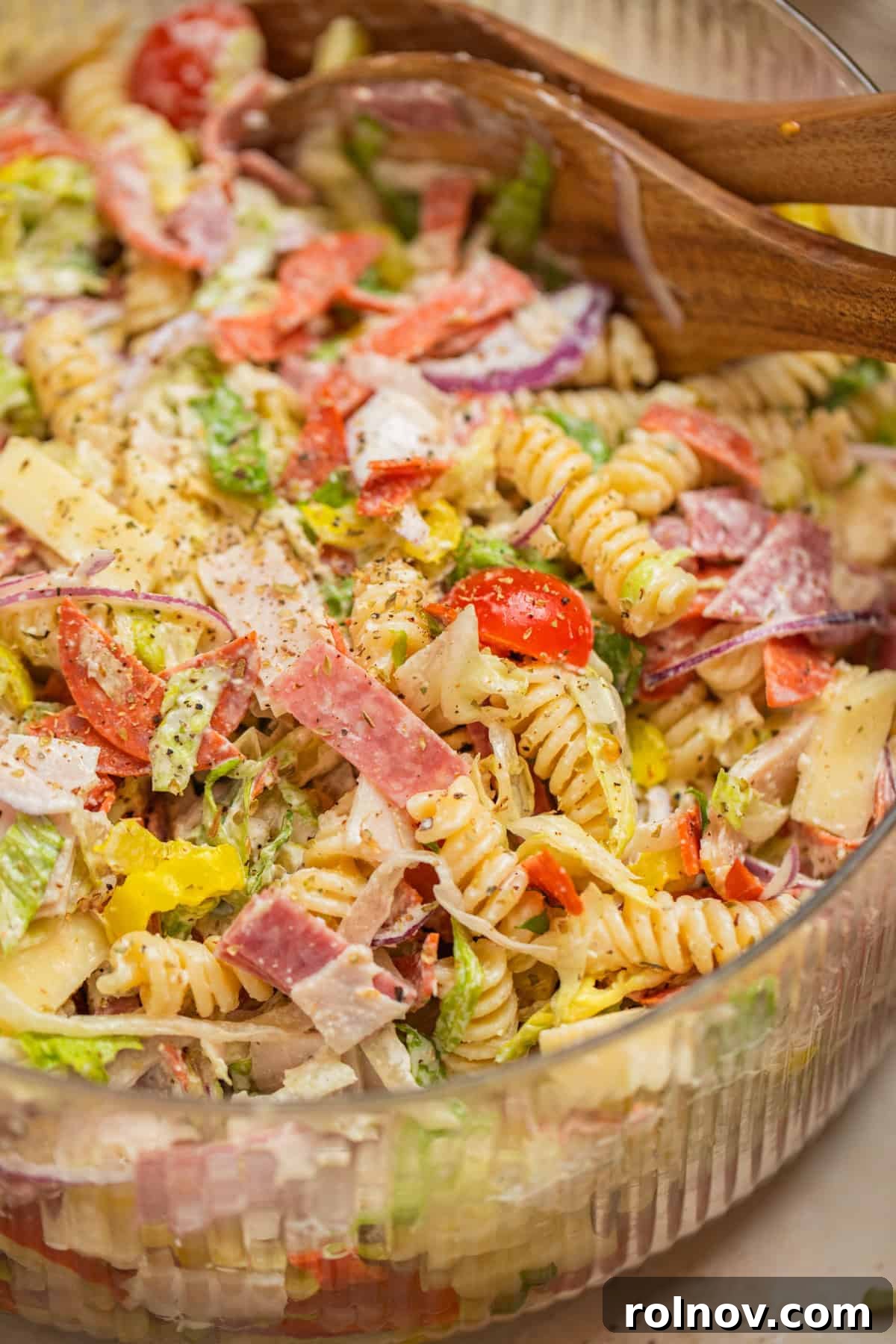 Loaded Grinder Pasta Salad 2 A large bowl filled with vibrant Italian Grinder Pasta Salad, featuring fusilli pasta, colorful vegetables, and deli meats, with serving utensils propped inside.