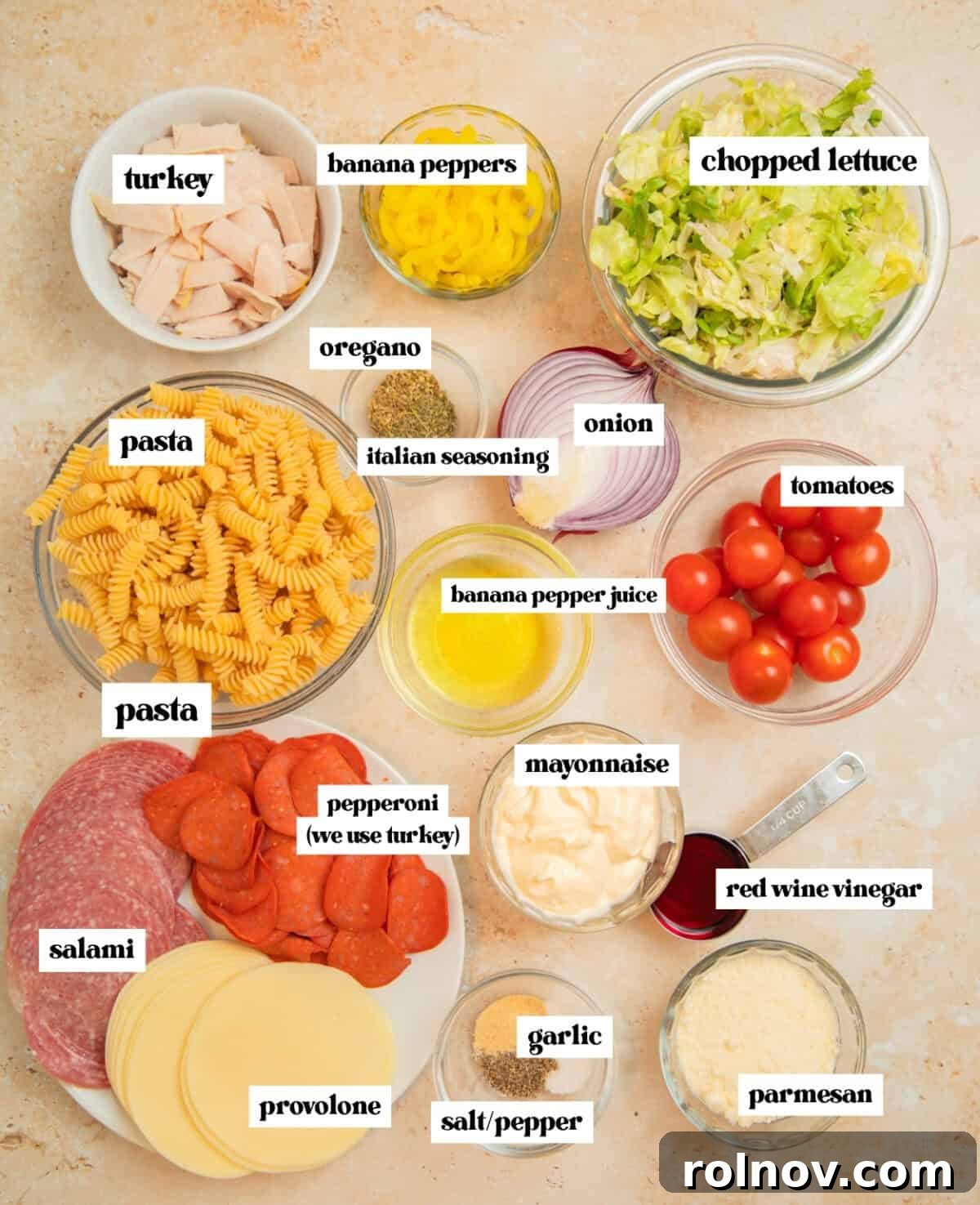 Loaded Grinder Pasta Salad 4 Individual ingredients for Italian Grinder Pasta Salad laid out: uncooked fusilli pasta, various deli meats, provolone cheese, grape tomatoes, banana peppers, and fresh lettuce.