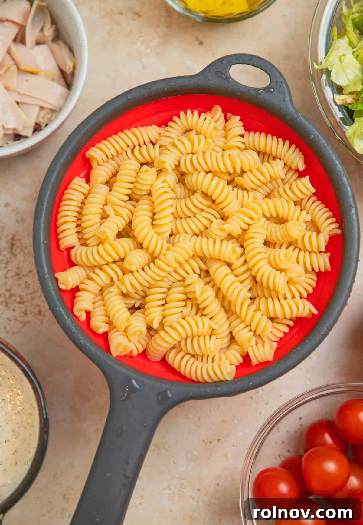 Loaded Grinder Pasta Salad 5 Cooked fusilli pasta being drained in a colander under cold running water.