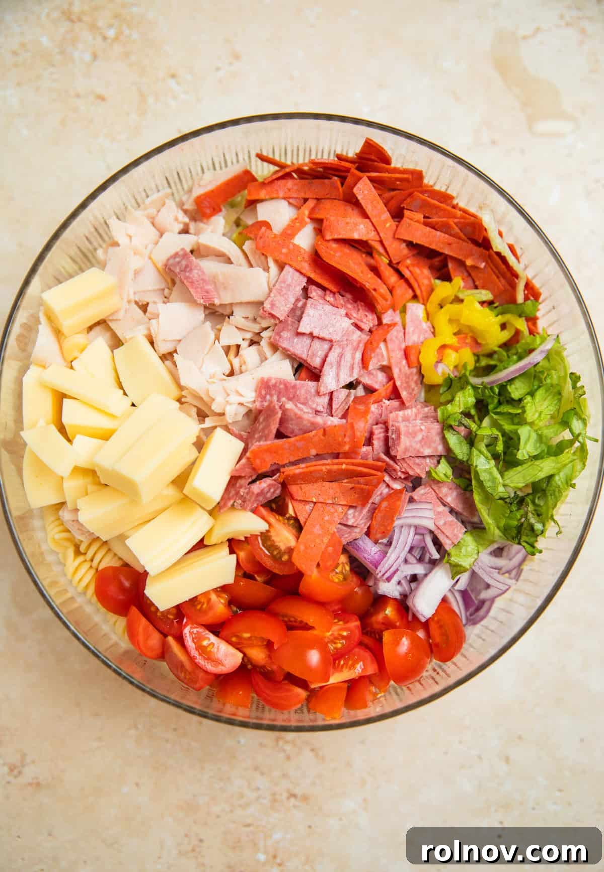 Loaded Grinder Pasta Salad 6 Chopped pasta salad ingredients including cooked pasta, shredded lettuce, banana peppers, provolone cheese, and various deli meats in a large mixing bowl.