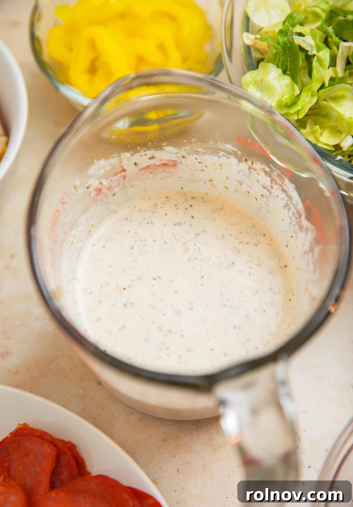 Loaded Grinder Pasta Salad 8 The creamy parmesan dressing, perfectly whisked and blended, in a clear mixing cup.