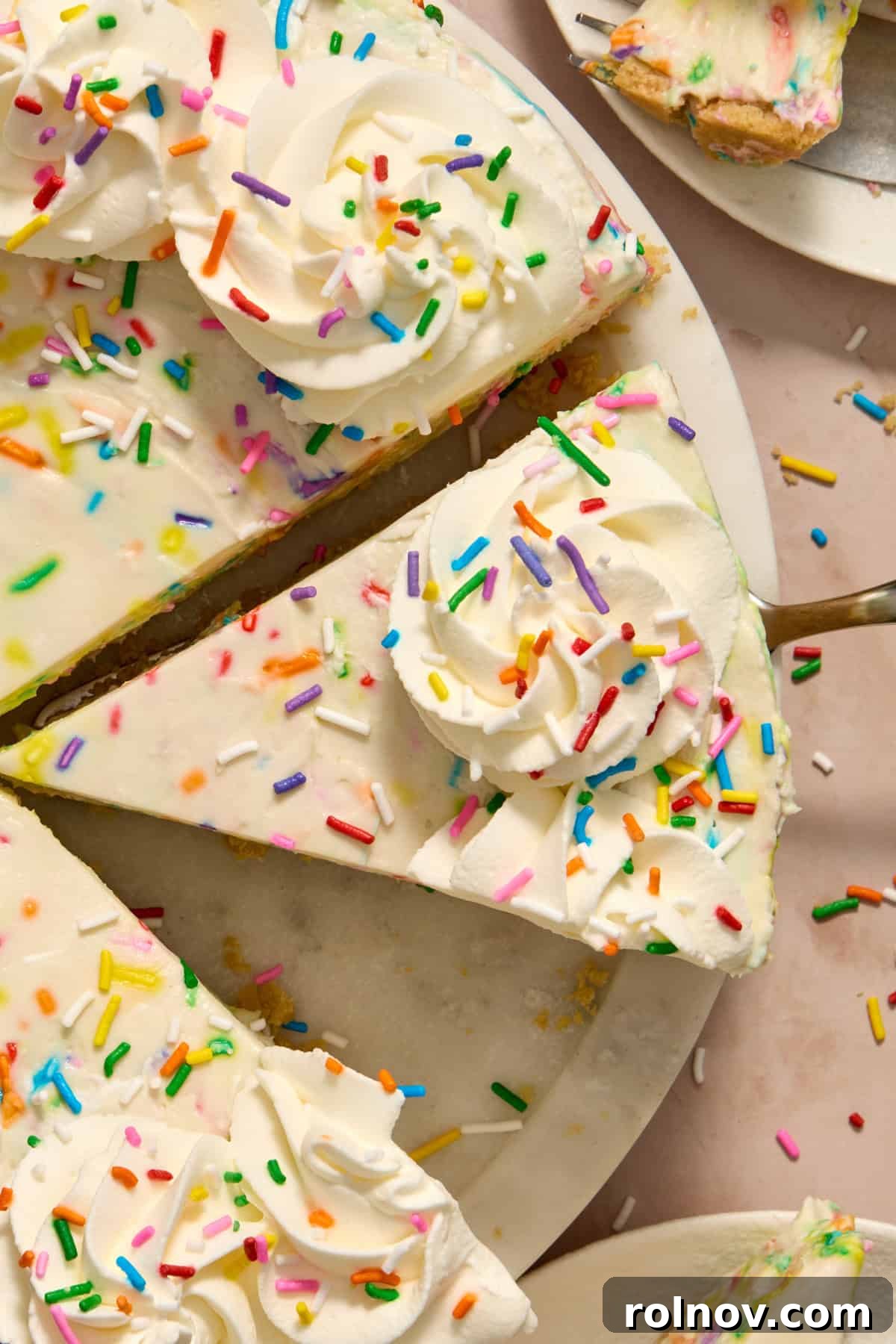 Overhead view of slices of funfetti cheesecake, garnished with whipped cream and sprinkles.