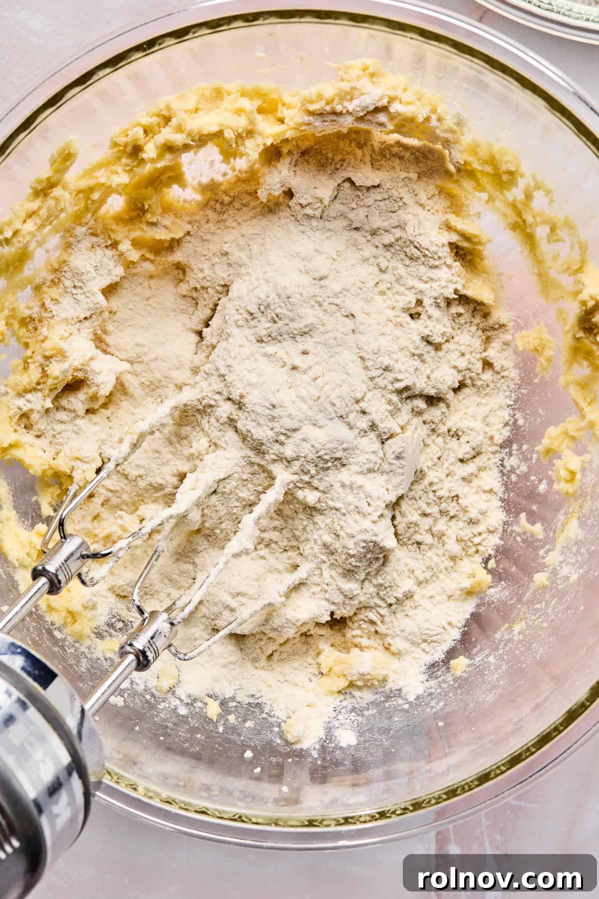 Frosted Sugar Delights 8 Dry ingredients are slowly added to the wet ingredients in a mixing bowl.