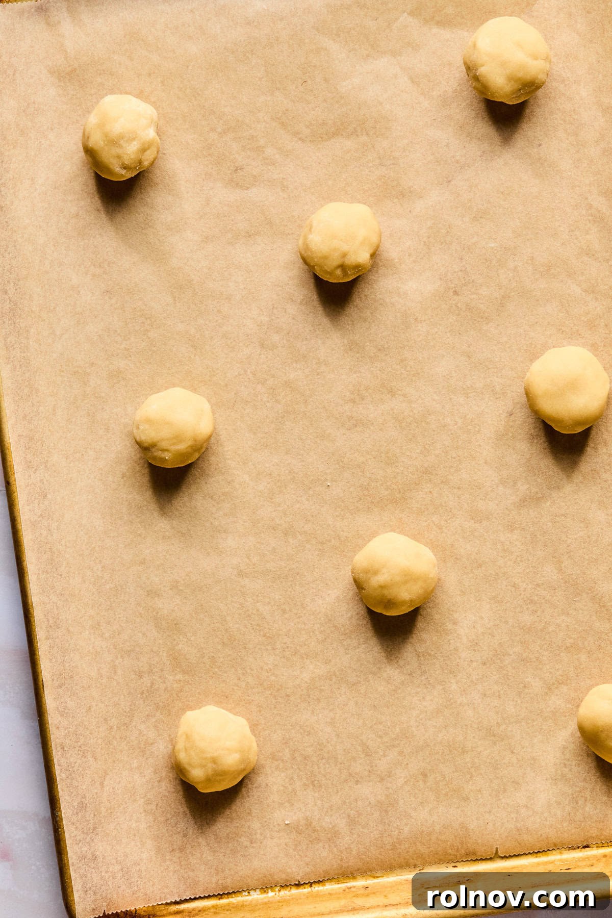 Frosted Sugar Delights 10 Sugar cookie dough balls arranged on a parchment-lined cookie sheet.
