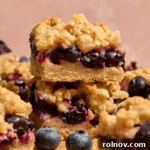 Stacked blueberry lemon bars with blueberries and other bars around it.