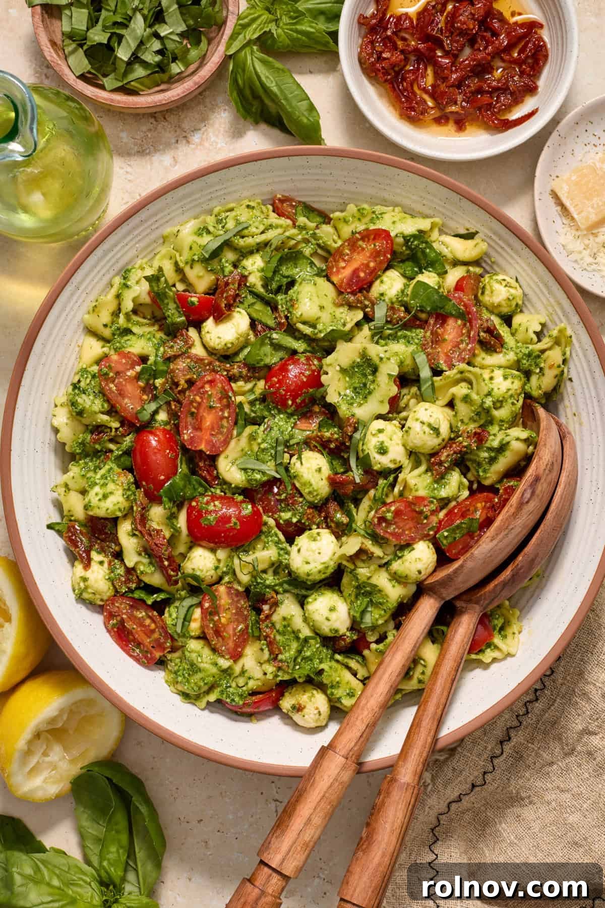 Serving bowl with tortellini pesto salad and salad serving utensils.
