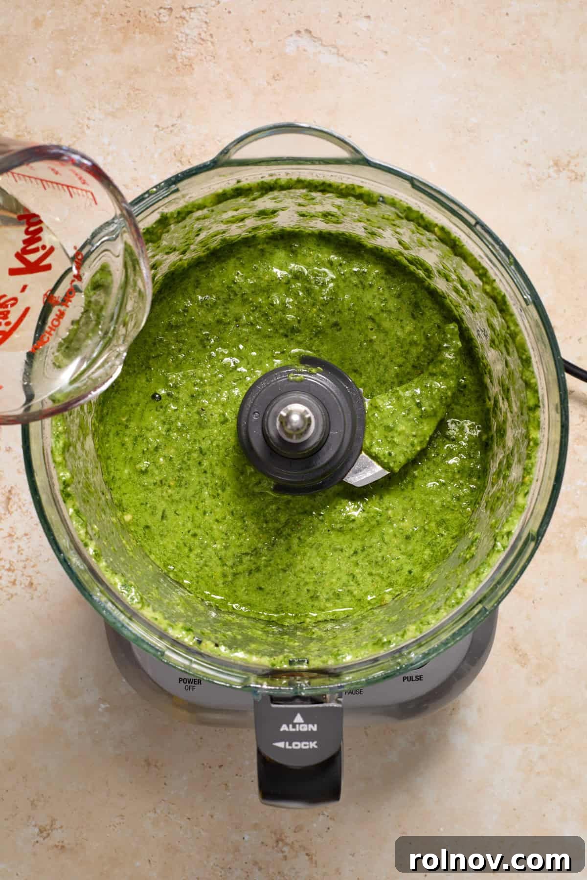 Olive oil being poured into pesto mixture in food processor.