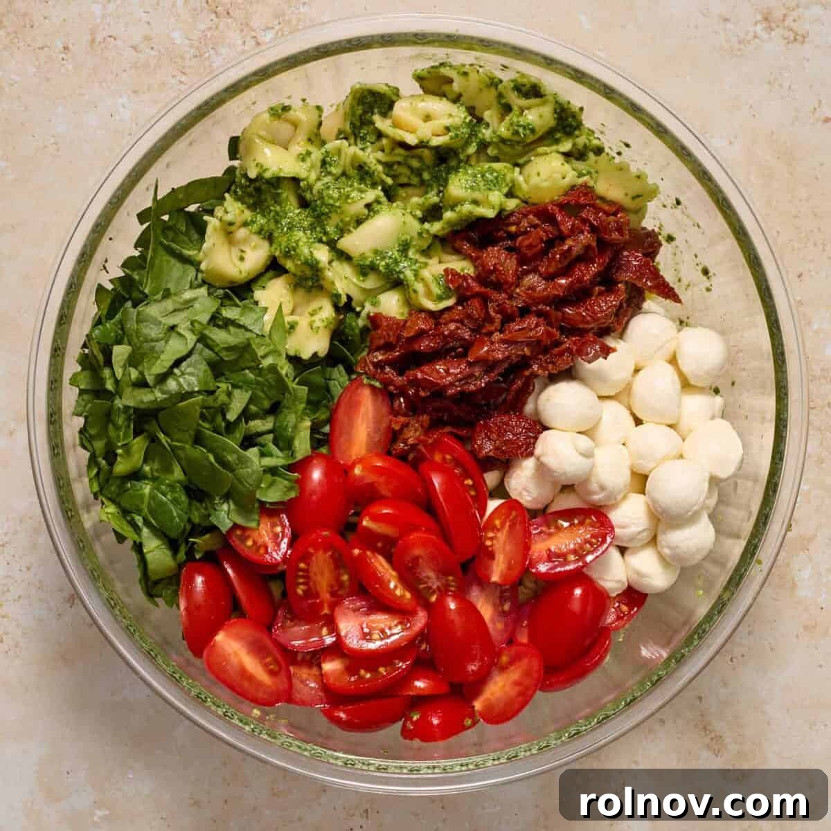 Tomatoes, spinach, mozzarella and other ingredients added to bowl with tortellini.