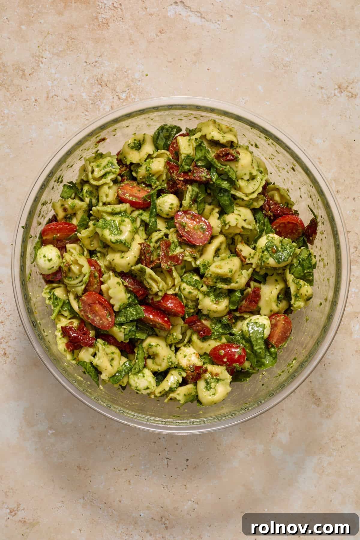 Prepared tortellini pesto pasta salad in mixing bowl.
