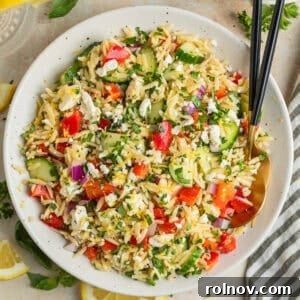 Lemon orzo salad with cucumber, bell pepper and feta in serving dish with serving utensils.