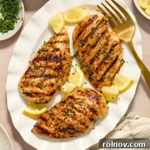 Grilled lemon pepper chicken on white serving platter with lemon wedges.