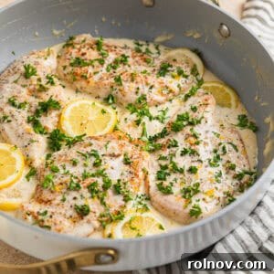 Creamy lemon chicken in skillet with lemon slices, cream cheese sauce and chopped parsley over top.