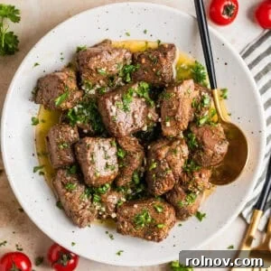 White plate with air fryer steak bites in lemon garlic butter sauce with fresh parsley over top.