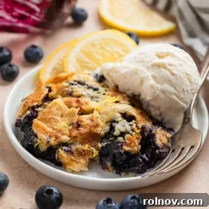 Blueberry lemon dump cake on white plate with fork and scoop of vanilla ice cream.