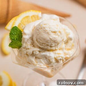 Scooped lemon ice cream in stemware with two lemon quarters and fresh mint leaves.