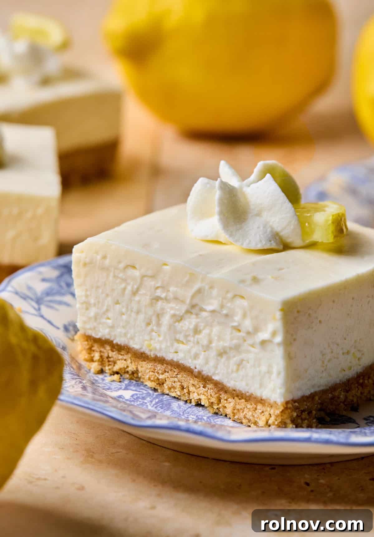 No-Bake Lemon Cheesecake Bars Recipe — Creamy Citrus Dessert 2 Lemon cheesecake bar on plate with whipped cream and lemon slice on top.