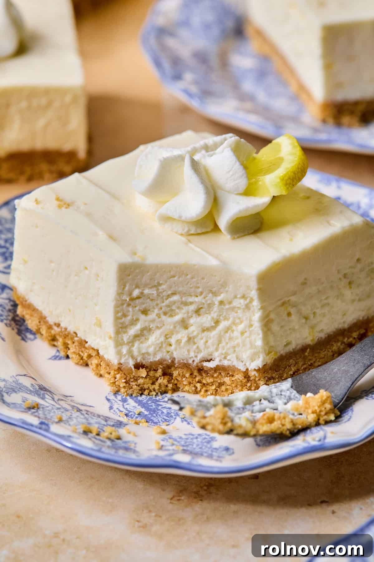 No-Bake Lemon Cheesecake Bars Recipe — Creamy Citrus Dessert 15 Slice of no-bake lemon cheesecake bar on plate with forkful taken out to show texture.