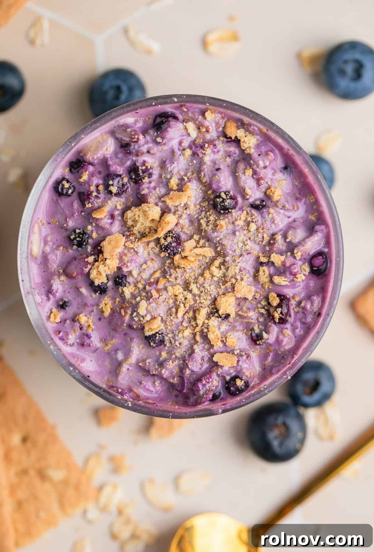Overhead view of blueberry cheesecake overnight oats in glass topped with crushed graham crackers.