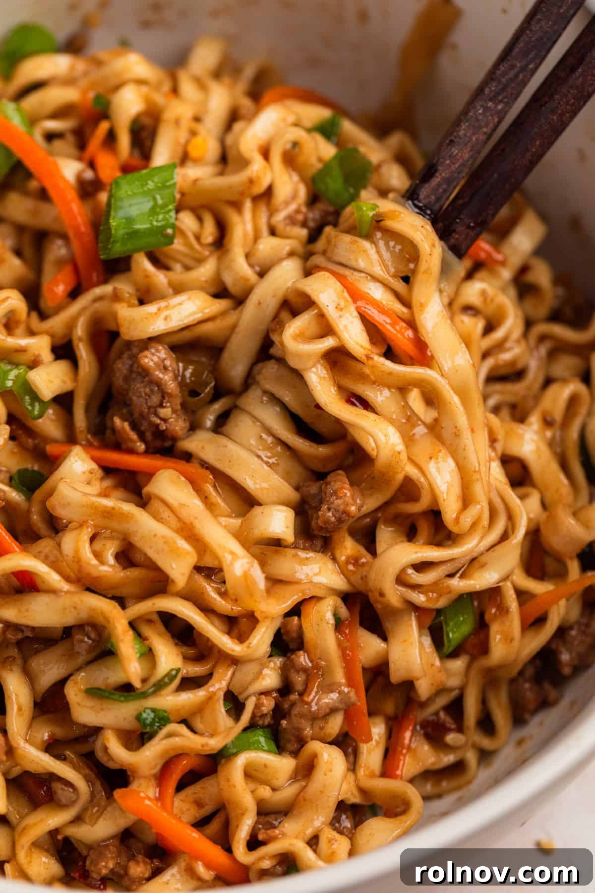 Beef noodles on chopsticks in bowl.