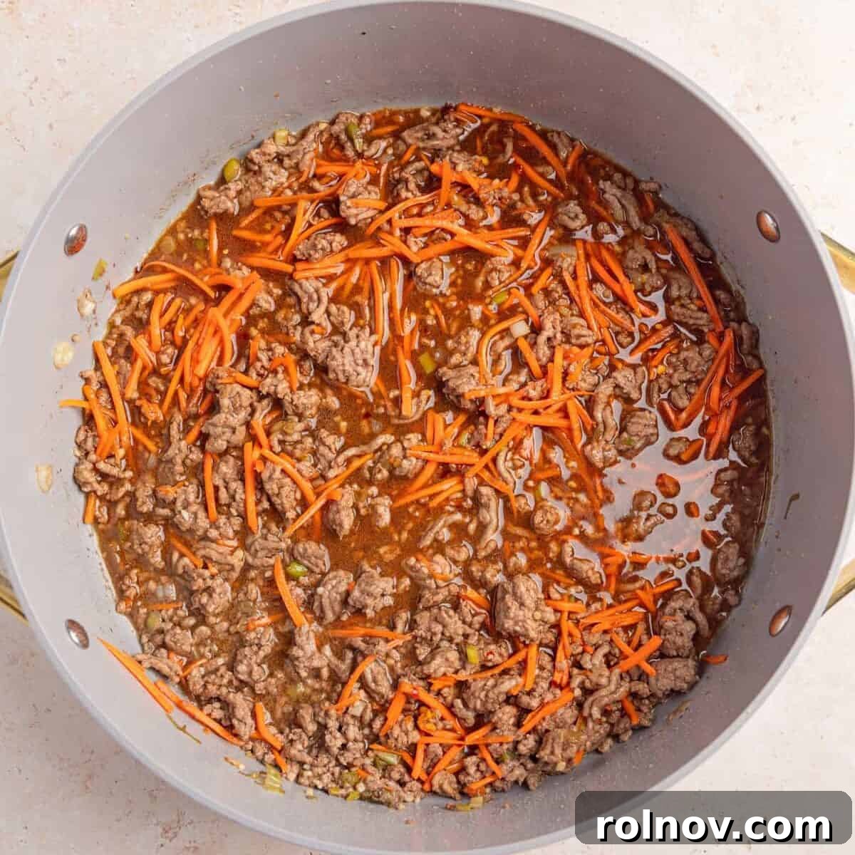 Browned ground beef with carrots and sauce added to pan.
