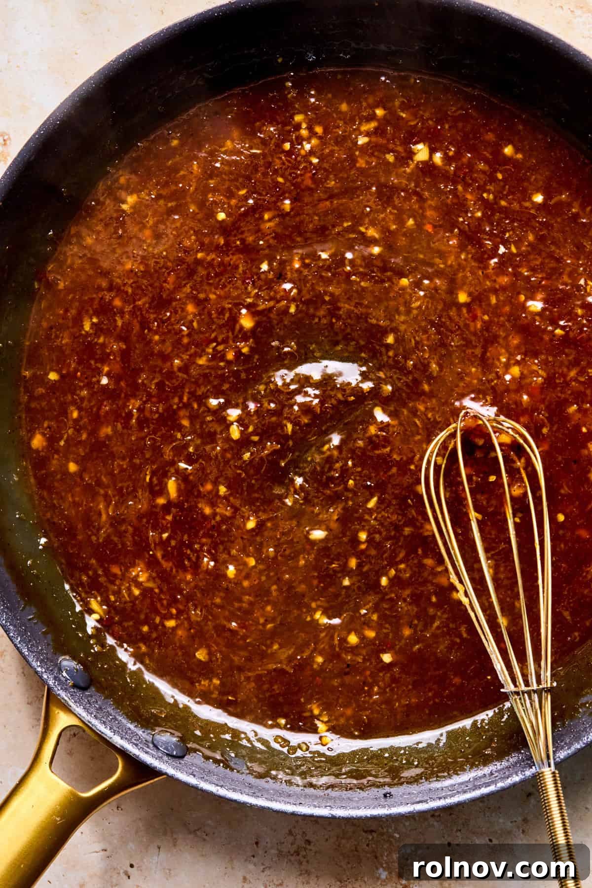 Cooked spicy orange sauce in skillet with whisk.