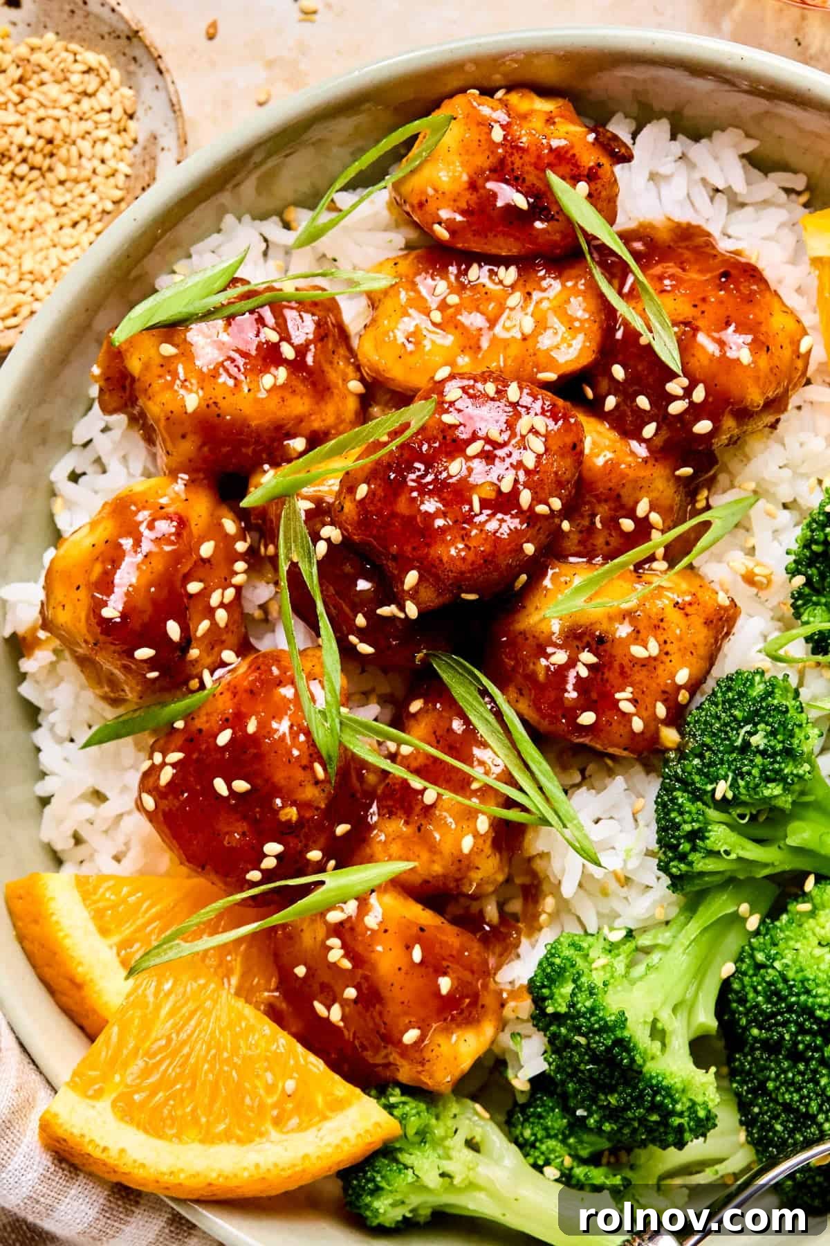 Orange chicken over rice topped with scallions and sesame seeds.