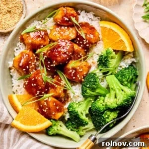 Spicy orange chicken over rice with broccoli and orange slices.