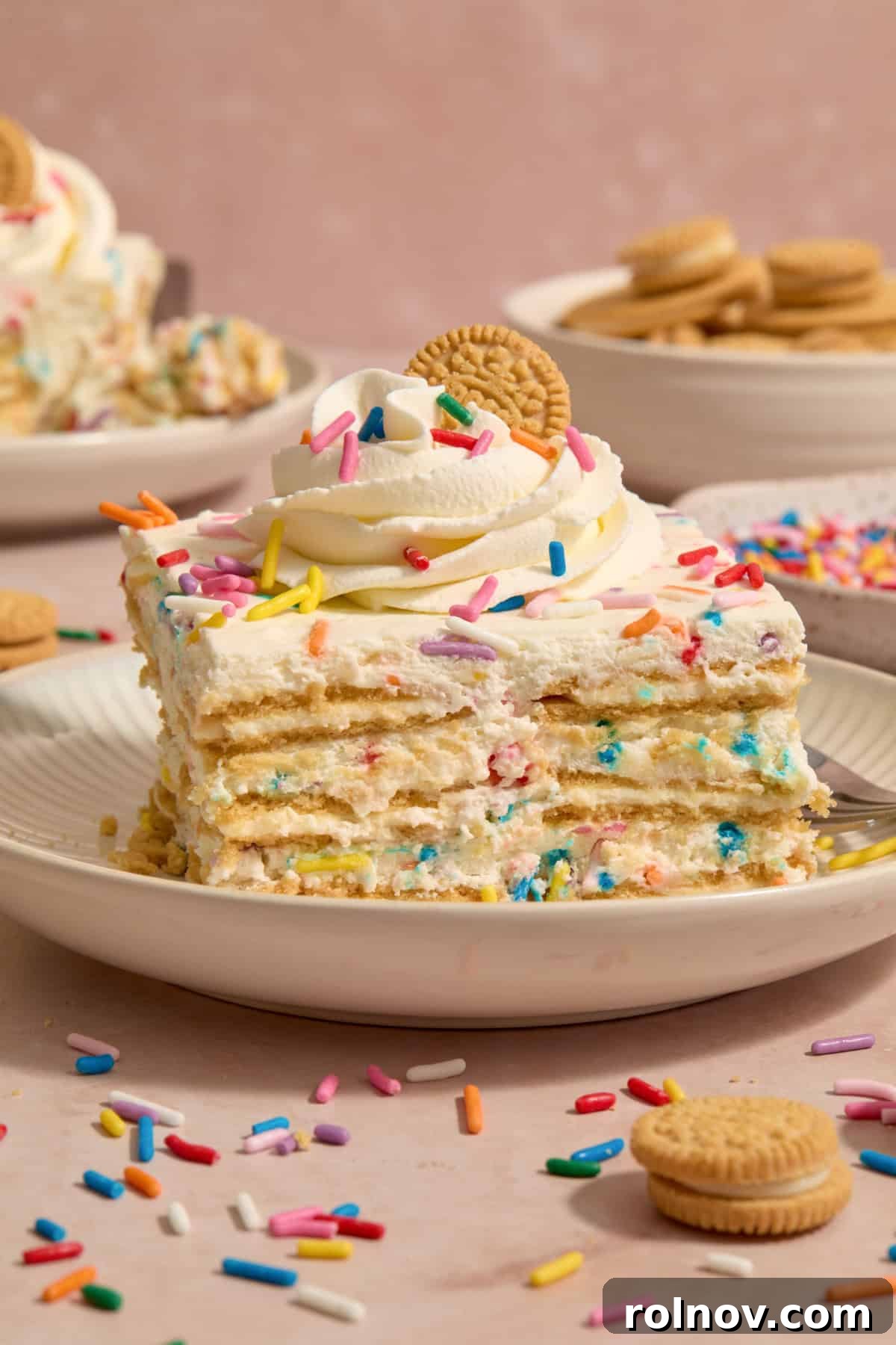 Slice of no-bake funfetti icebox cake topped with whipped cream and mini golden Oreo.