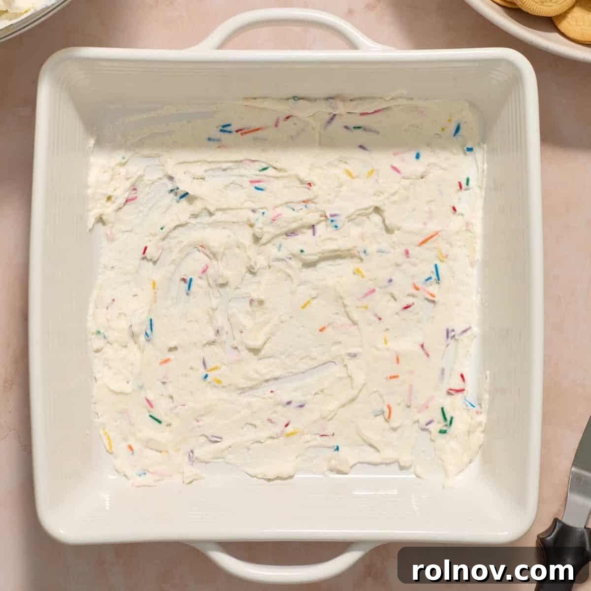 Funfetti whipped cream mixture spread on the bottom of square pan.