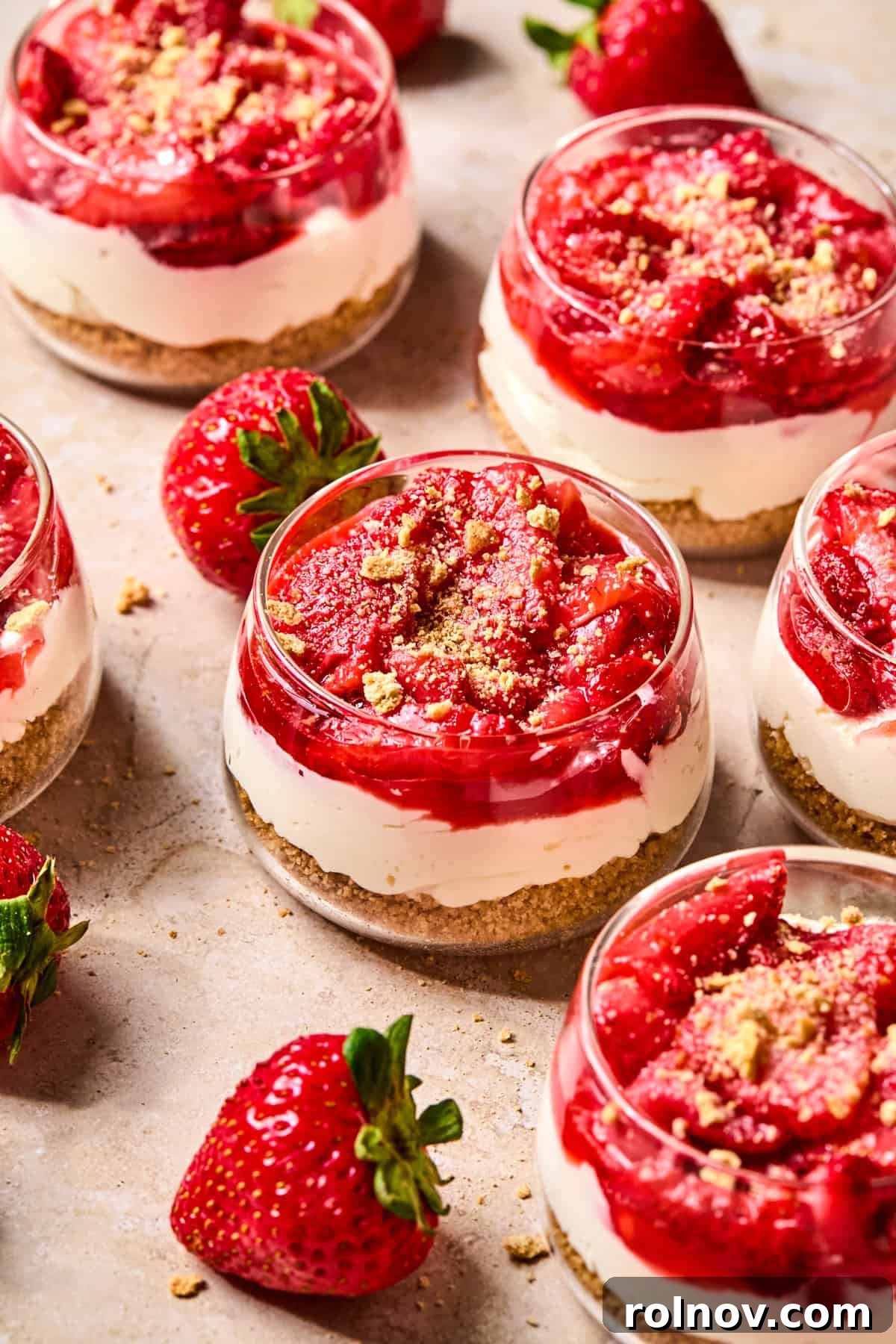 Roasted Strawberry Mini Cheesecake Cups Recipe 2 Strawberry topped no-bake cheesecake cups with strawberries beside the cups.
