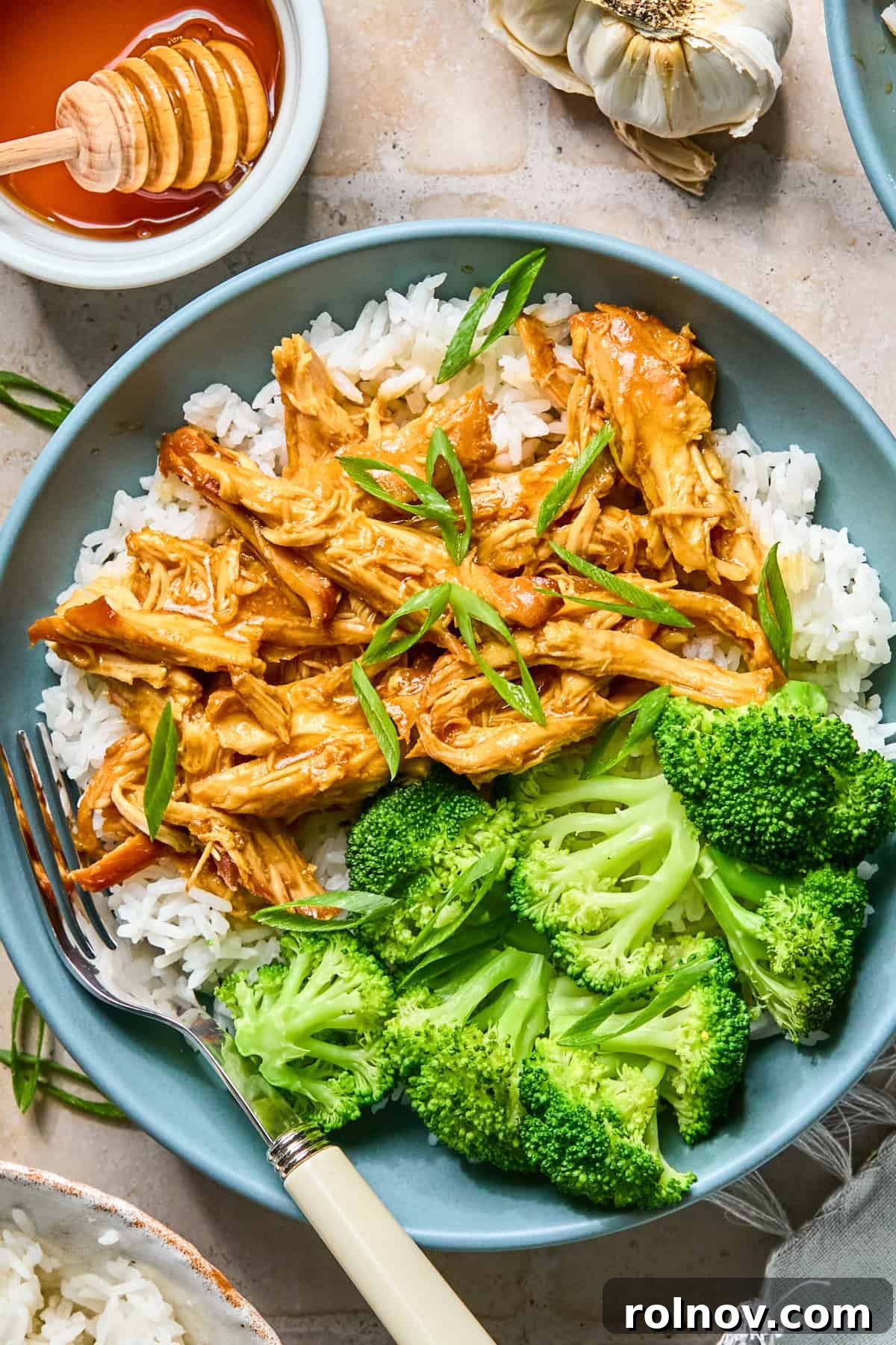 Sticky Honey Sriracha Slow Cooker Chicken 2 Slow cooker honey garlic sriracha chicken in dish over rice with broccoli.