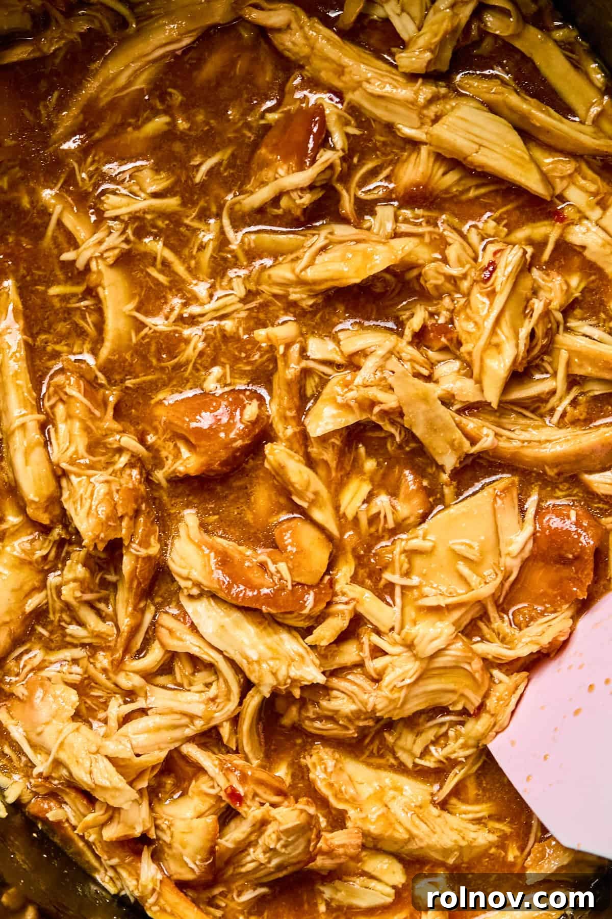 Sticky Honey Sriracha Slow Cooker Chicken 11 Close up view of slow cooker with shredded honey garlic and sriracha chicken with spoon.
