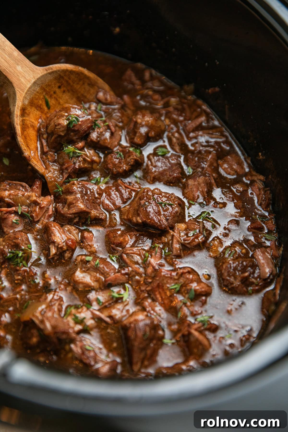 Wood spoon scooping into crockpot with beef tips.
