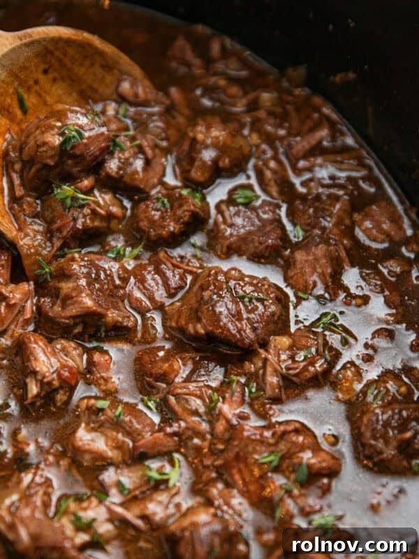 Crockpot with beef tips in gravy with wooden spoon.