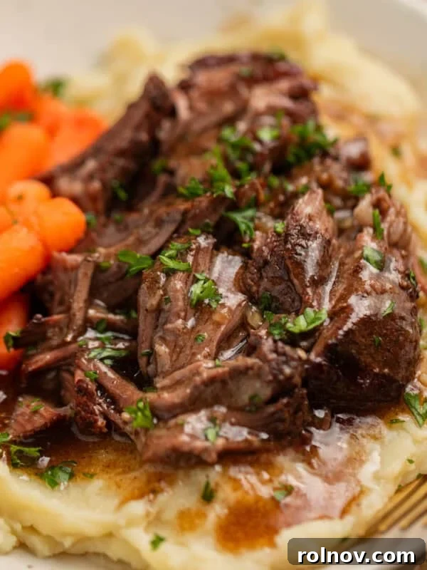 Short ribs with gravy over top on plate with potatoes and carrots.