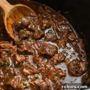 Crockpot with beef tips in gravy with wooden spoon.