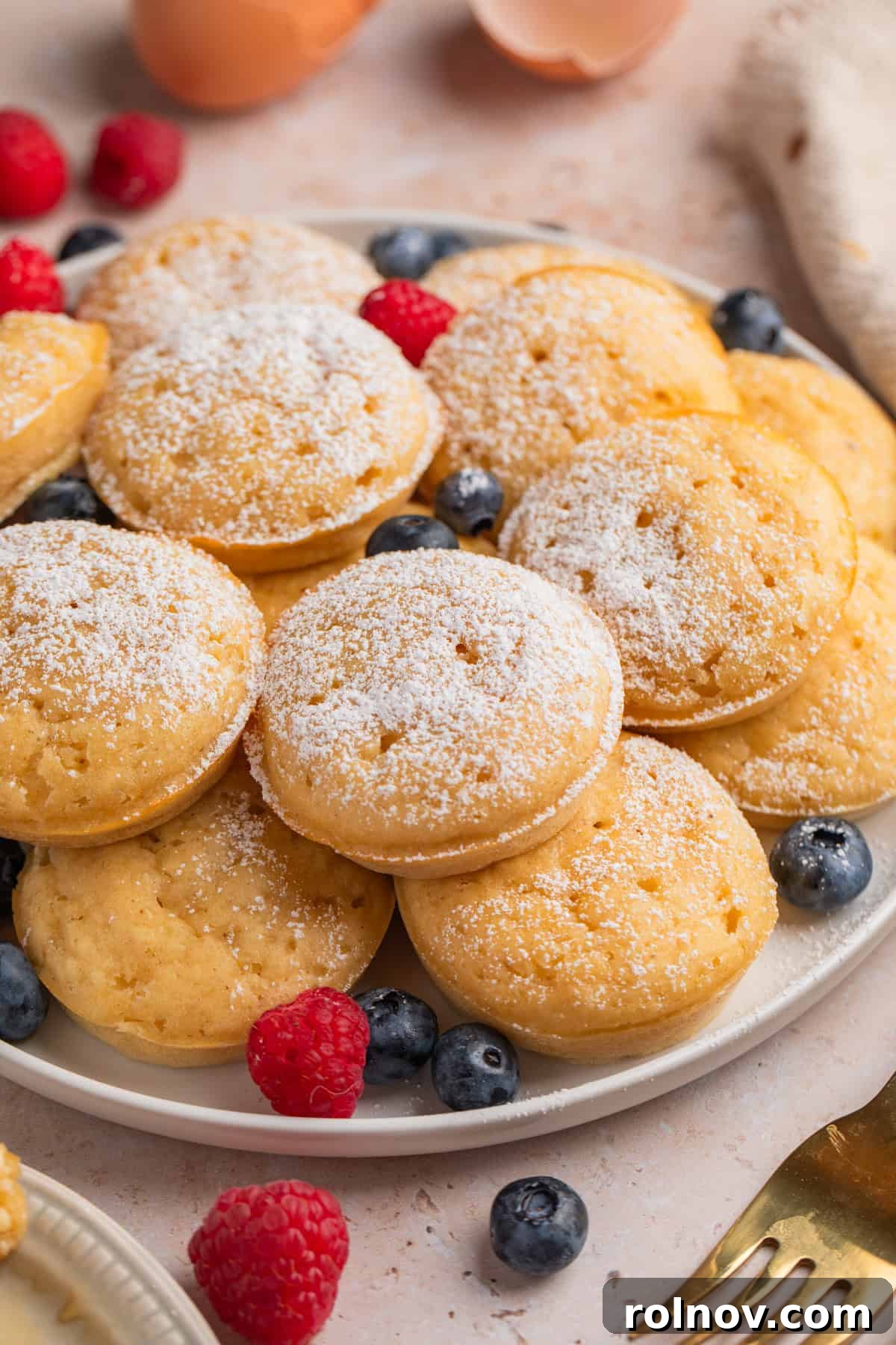 Pancake bites on plate with berries dusted with powdered sugar.
