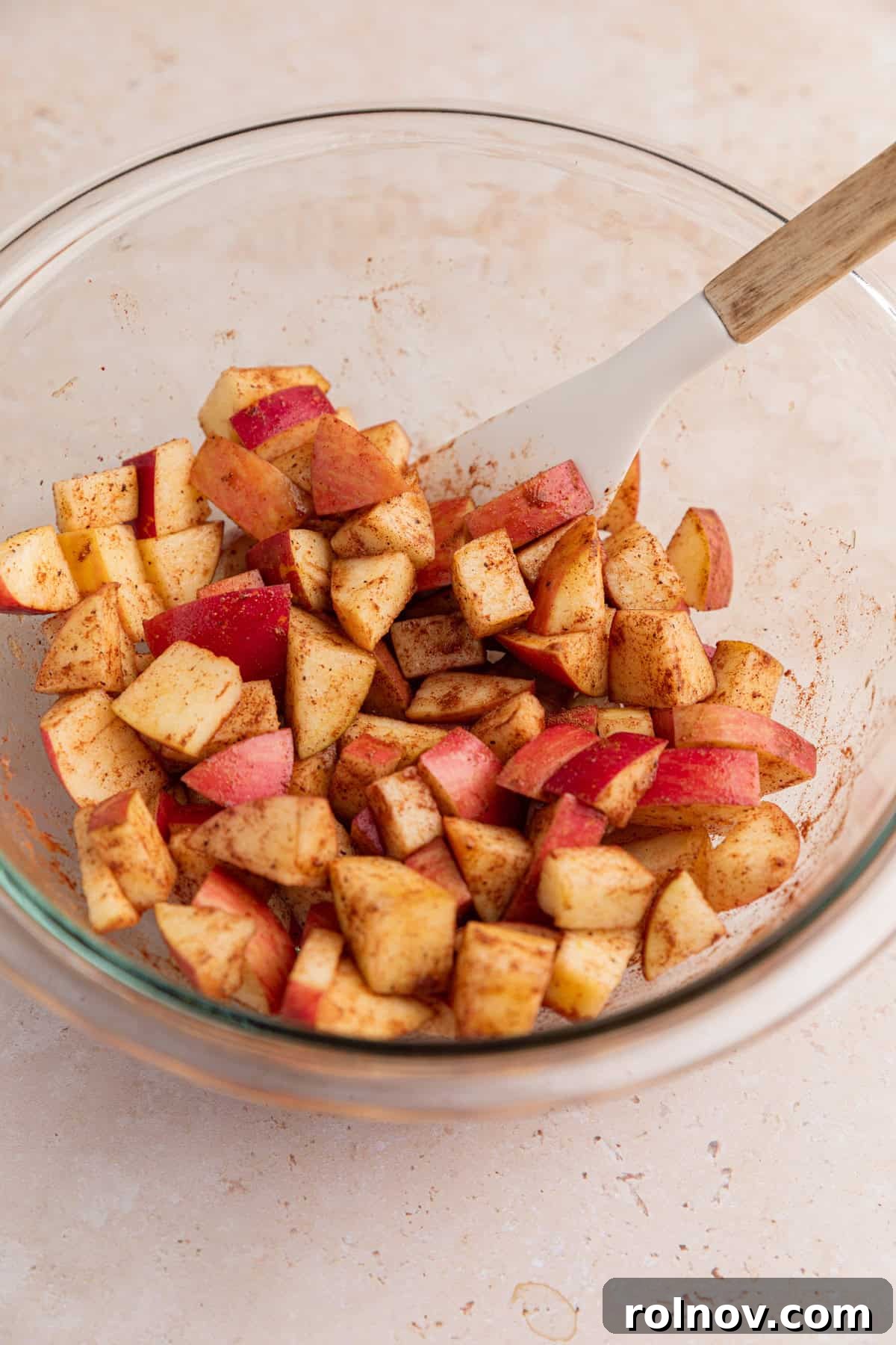 Sheet-Pan Apple Pancakes with Cinnamon 4 Chopped apples with cinnamon and maple syrup in glass bowl with spatula.