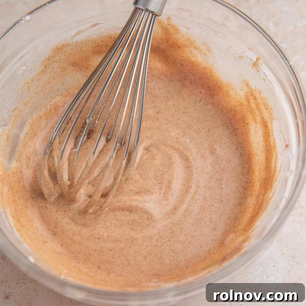 Cinnamon icing in bowl with whisk.