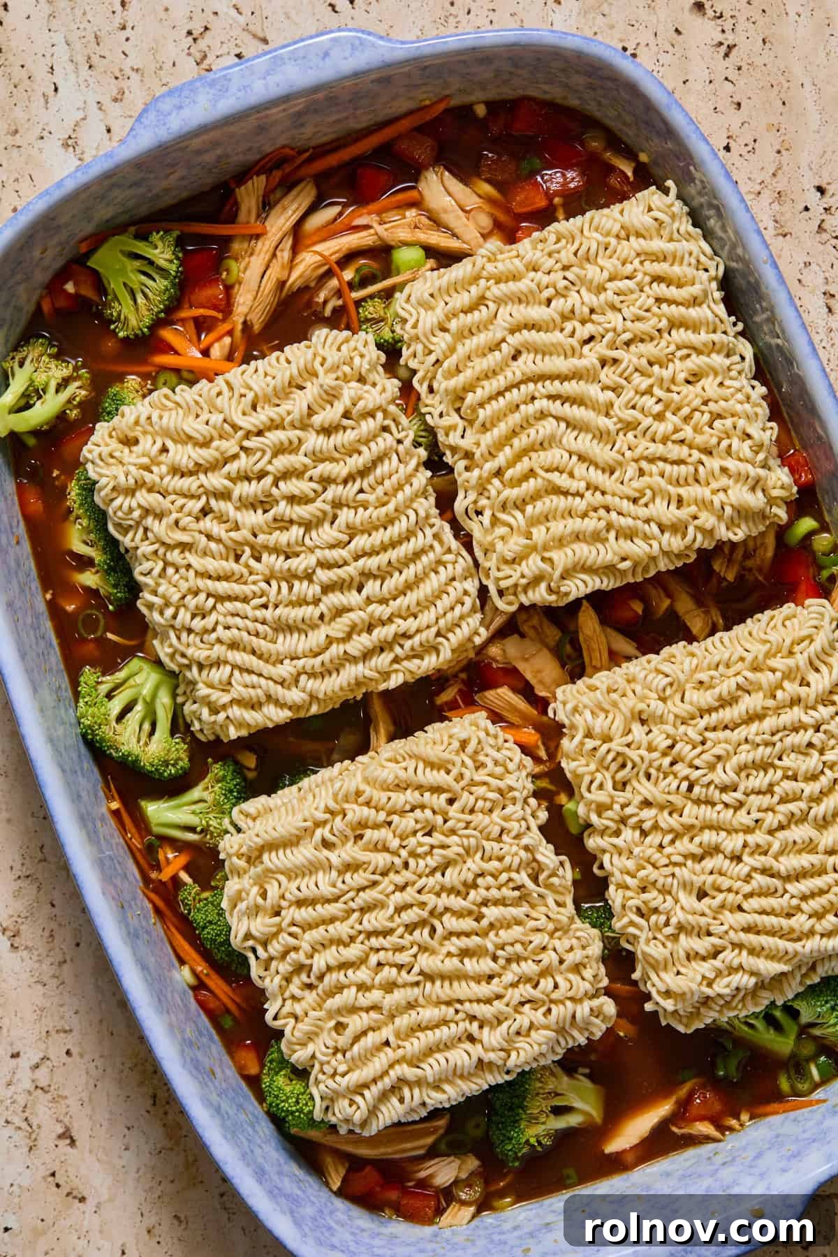Ramen bricks on top of veggies and sauce in pan before baking.
