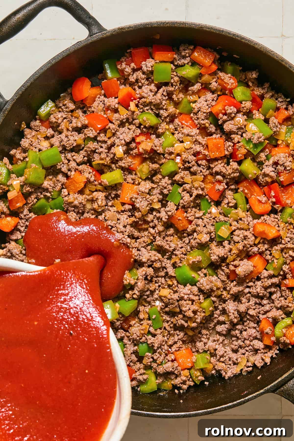 Cheesy Sloppy Joe Casserole for Family Weeknight Dinners 8 Browned ground beef and peppers with tomato mixture being poured in.