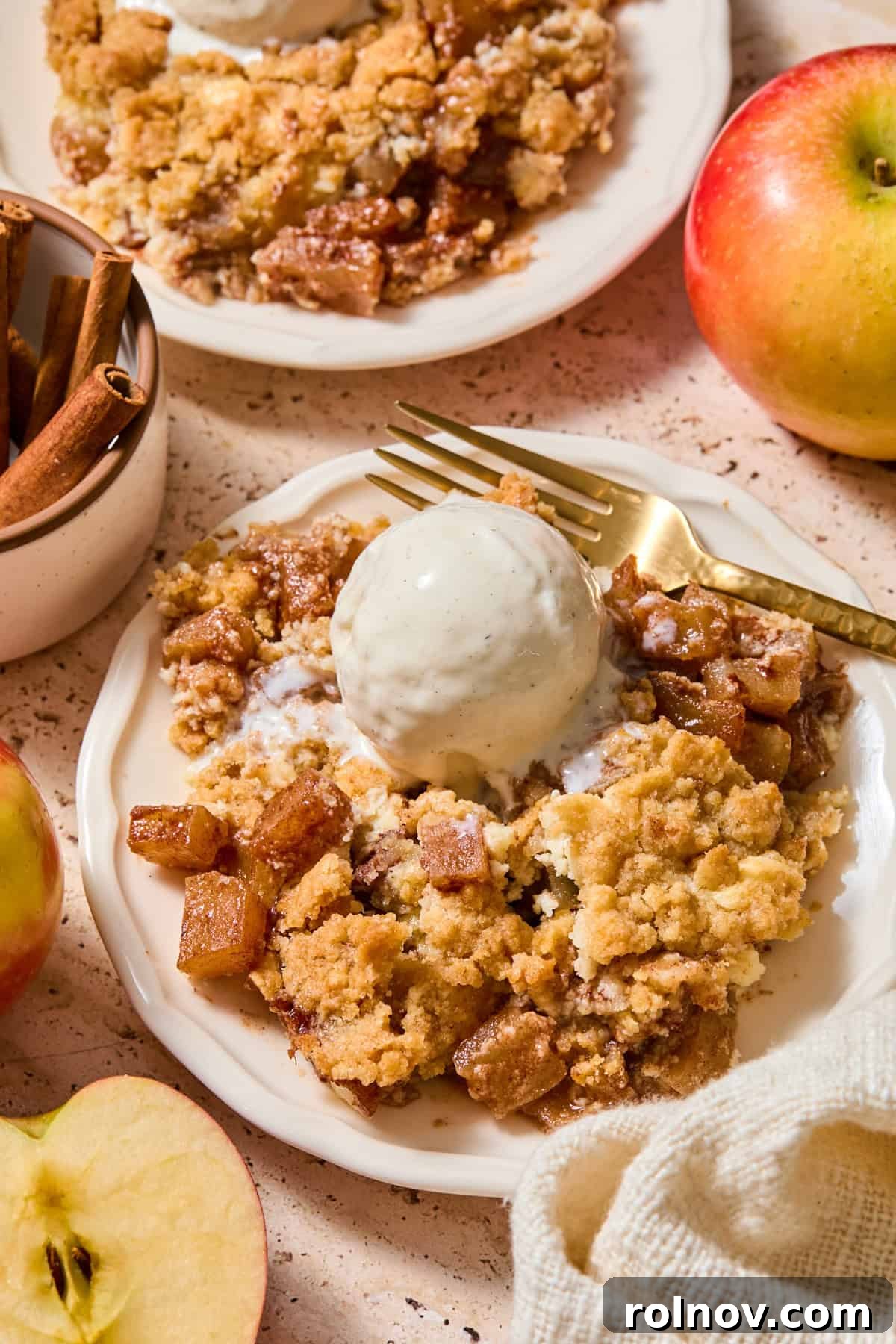 Cream cheese apple cobbler on plate with scoop of vanilla ice cream over top.